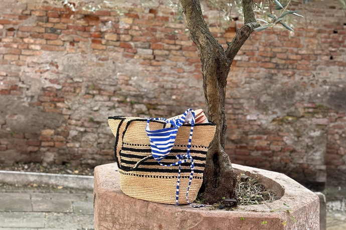 lemlem hand crocheted raffia bag with lemlem swimwear coming out of it next to an olive tree.
