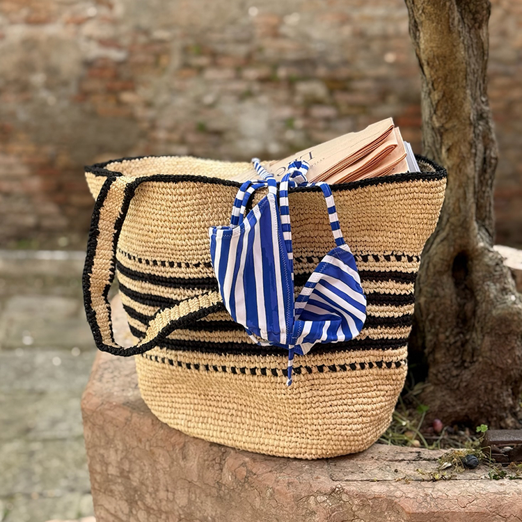 lemlem hand crocheted raffia bag with lemlem swimwear coming out of it next to an olive tree.