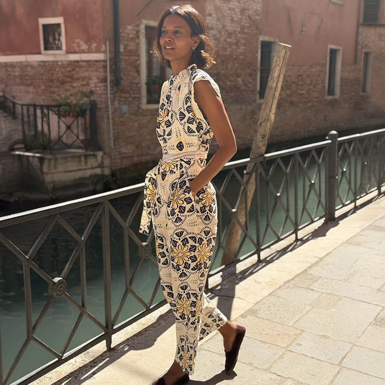 Liya Kebebe walking in Venice wearing a lemlem linen crop top and matching linen high waist pants in white with blue and yellow tile prints. 