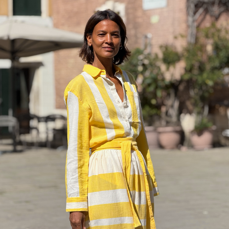Liya Kebebe walking in Venice wearing a lemlem hand woven button down shirt and matching lemlem handwoven skirt in white and yellow stripes. 