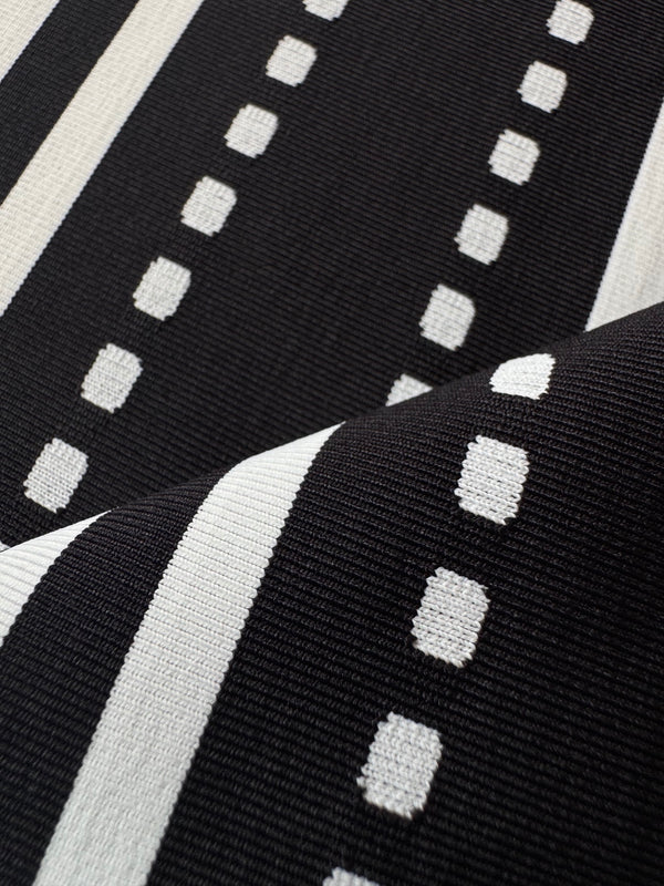 Close-up of a black knit fabric with white stripes and rows of small white rectangular dots, shown in soft folds.