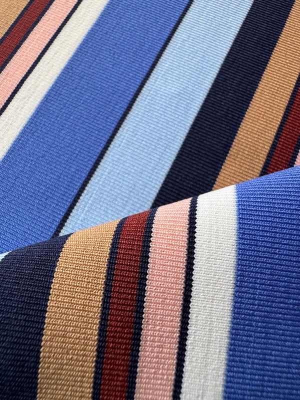 A close-up of a striped lemlem swim fabric with vertical bands of blue, navy, beige, white, pink, and red, shown folded to highlight the texture.