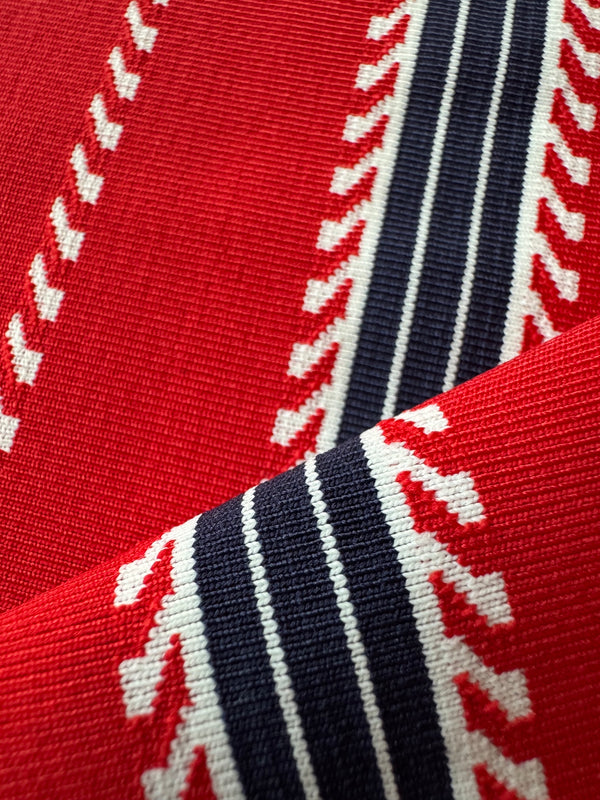 A close-up of a woven textile with a bold geometric pattern in red, navy blue, and white, showing the detailed knit texture and folded fabric layers.