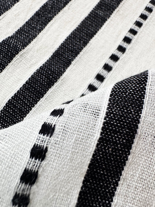 Close-up of a woven textile with bold black and off-white vertical stripes and dotted stripe accents, showing the fabric texture in soft folds.