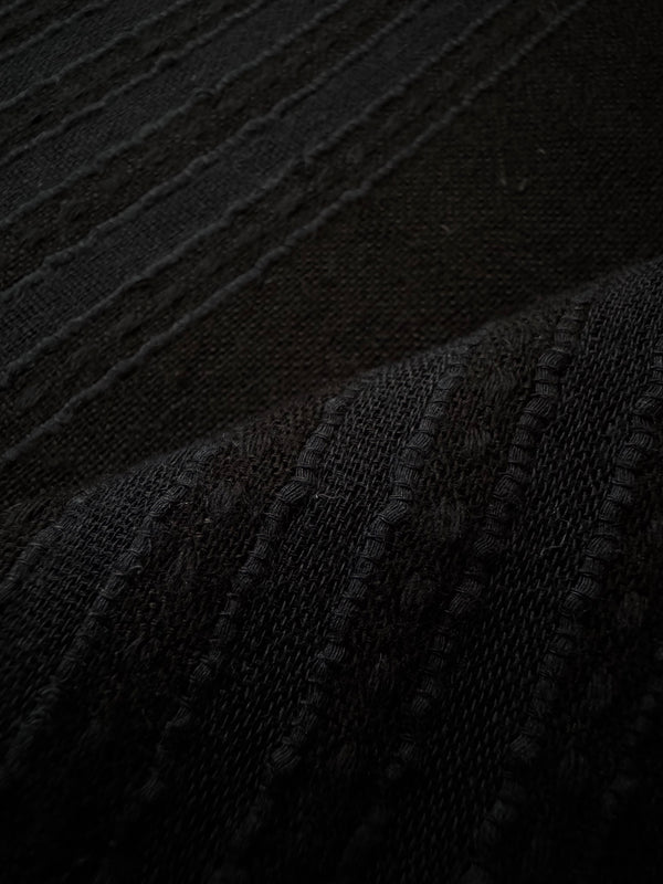 Close-up of a dark woven textile with a ribbed, textured pattern and soft fold shadows.