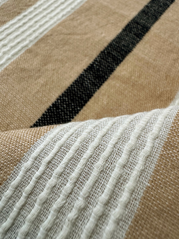 Close-up of a woven textile with a beige base, white textured stripes, and a bold black diagonal stripe.