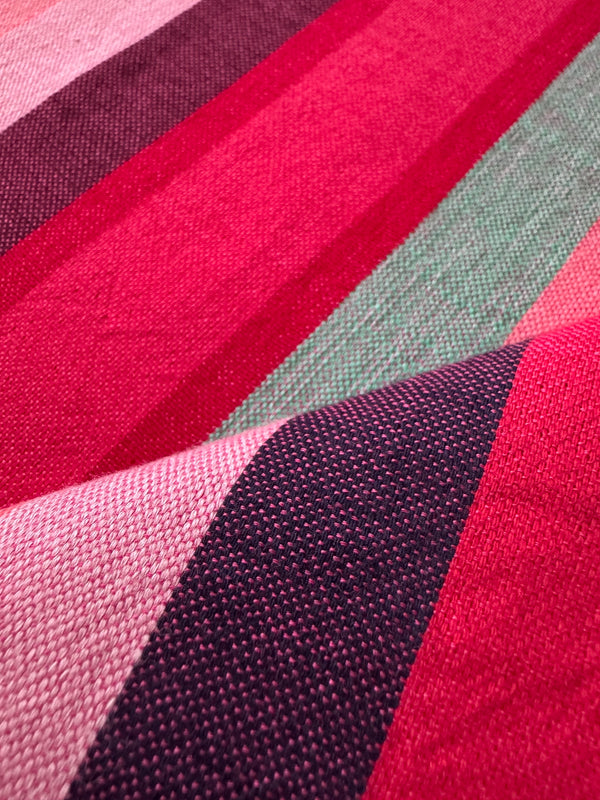 A close-up of a handwoven lemlem fabric with stripes in pink, magenta, deep purple, and sage green, showing the fabric texture in sharp detail.
