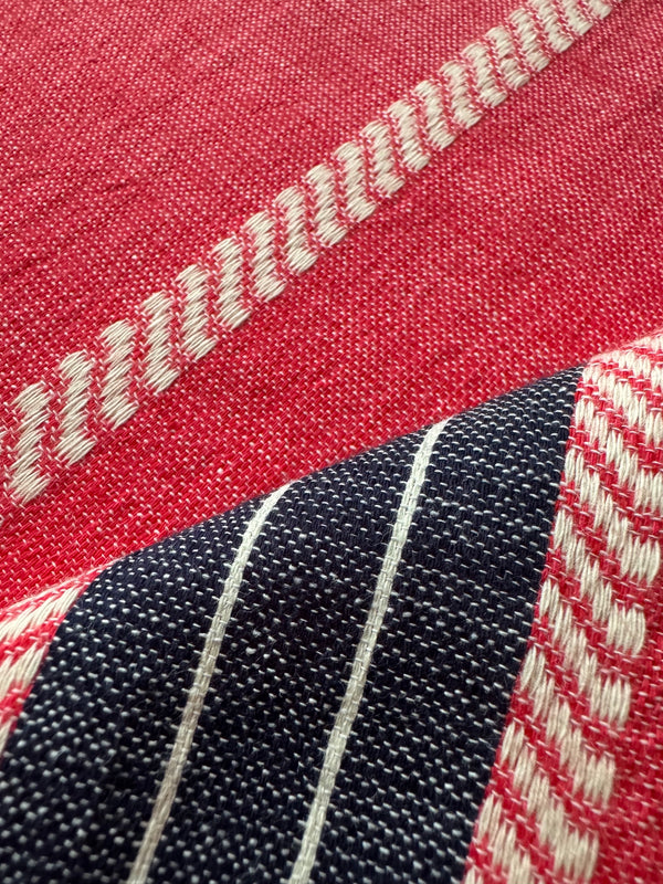 Close-up of a woven textile with a red field, a dark navy section with thin white stripes, and cream zigzag stitched detailing.