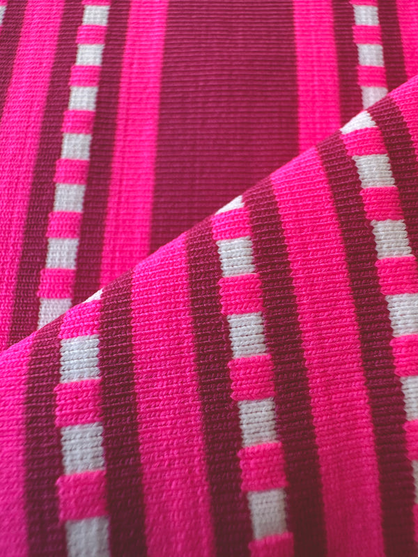 Close up on lemlem netifbi fuchsia fabric featuring vibrant bright pink stripes accented with ivory dots, all set against a bold fuchsia background