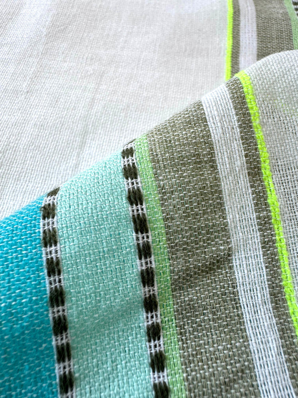 Close up on lemlem genet mint fabric featuring a chic stripe pattern in aqua blue and sage tones, delineated by dark olive dots and accented with a splash of neon yellow on a cream background.