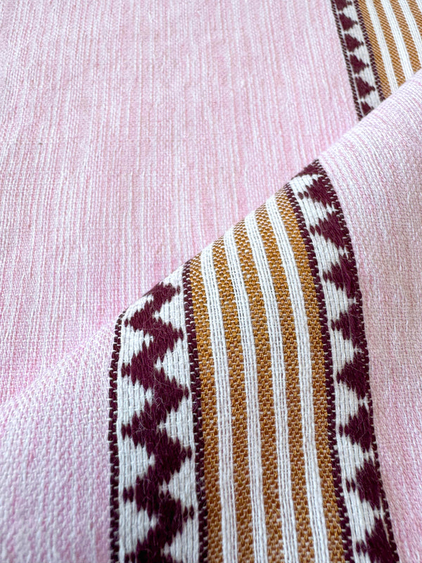 close up on lemlem handwoven fabric featuring detailed bands of deep burgundy, bronze, and pink stripes beautifully placed on a light cream 
