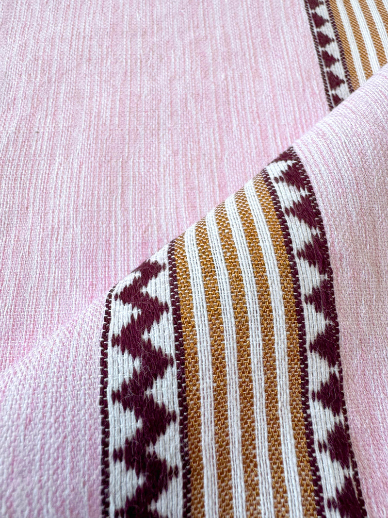 close up on lemlem handwoven fabric featuring detailed bands of deep burgundy, bronze, and pink stripes beautifully placed on a light cream 