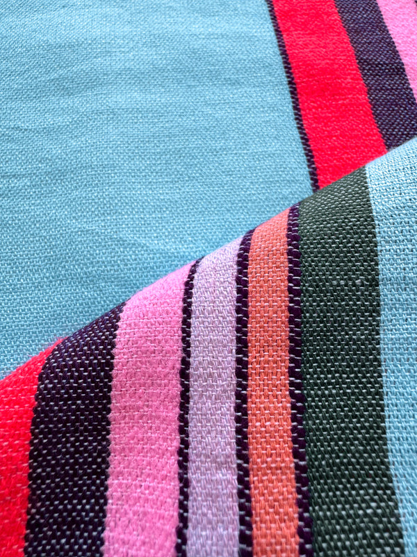 Close up on lemlem handwoven poppy sunset fabric featuring color block stripe pattern in white on sky blue background
