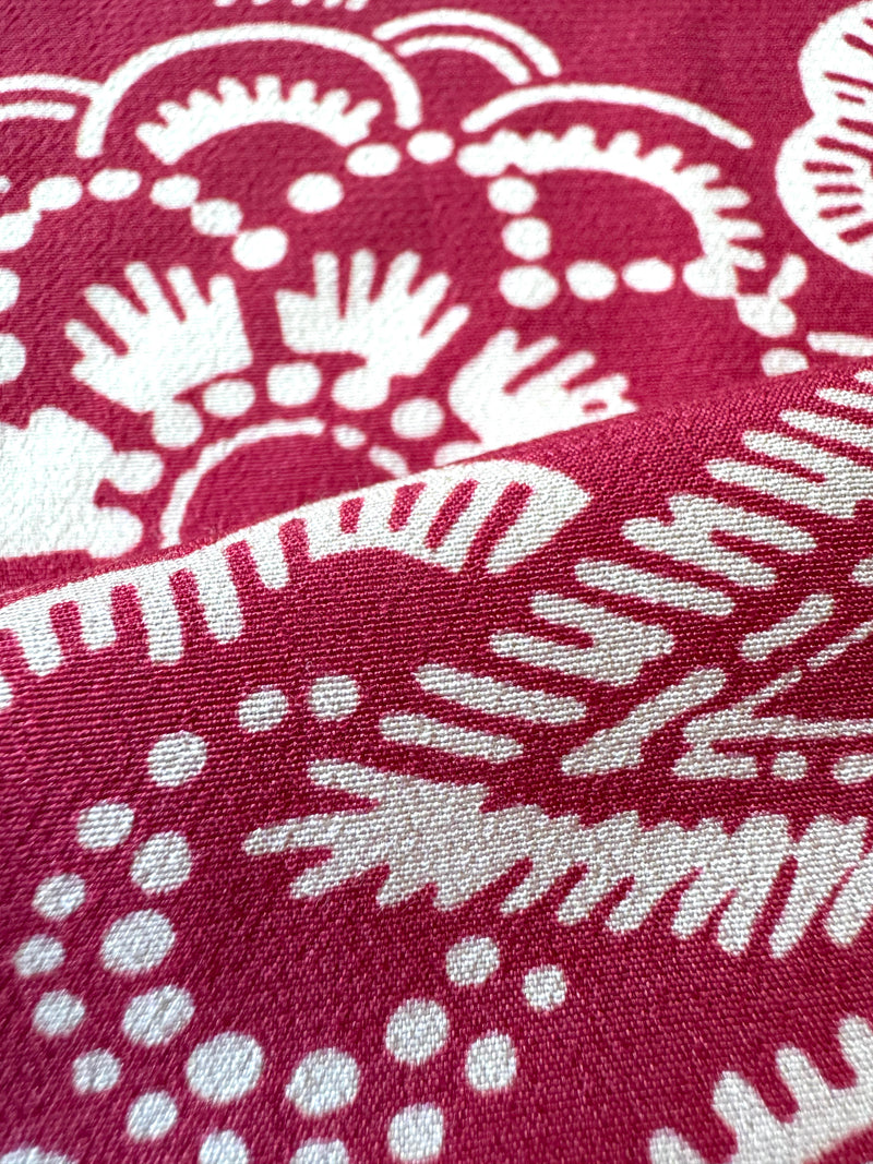 Close up on lemlem Maraki Ruby fabric featuring rich ruby-red fabric  adorned with intricate white floral and leaf motifs print