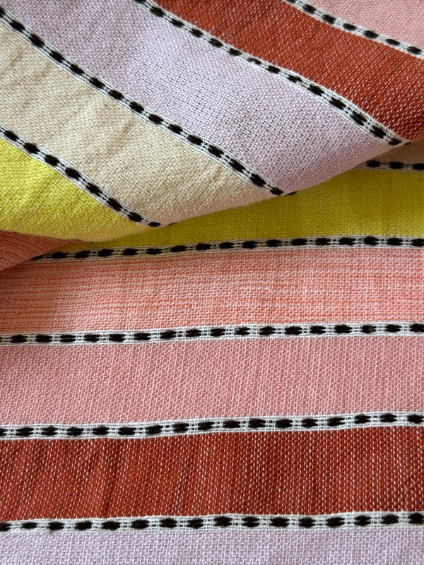 Close up on lemlem Mescel Citron fabric featuring soft sorbet-colored stripes in shades of peach, rust, and orchid, accented with a citrus yellow pop.
