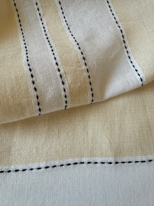 Close up on lemlem Debre Cream Fabric featuring bold stripes in bright white on a vanilla cream background, accented with navy pick stitch detailing