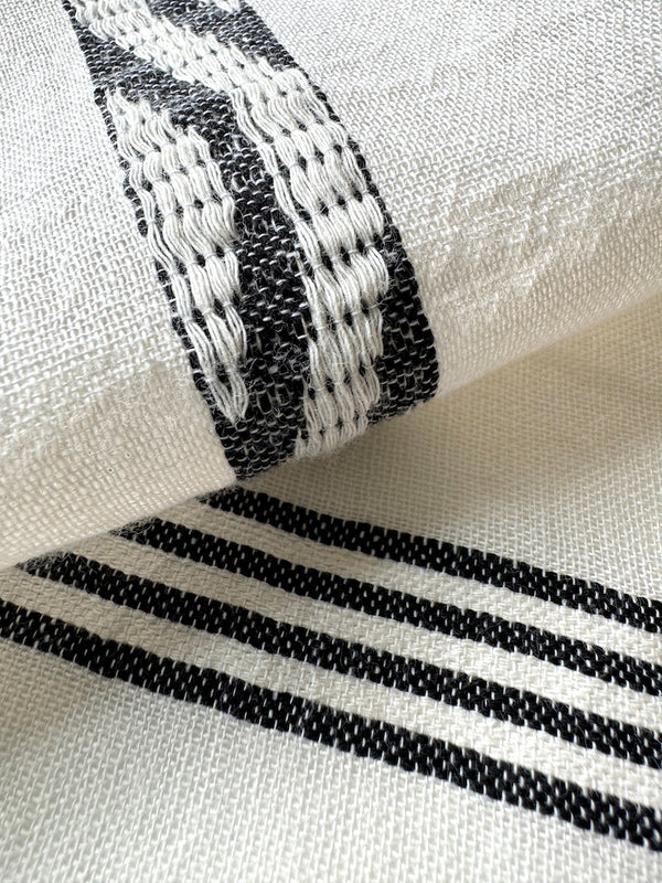 Close up on lemlem Besela Vanilla fabric featuring  black intricate stripes and a Tibeb wave band on a soft vanilla ground