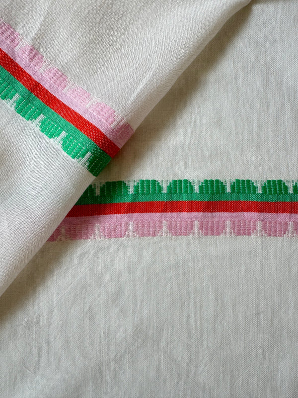 Close up on lemlem Kibebi Fragaria Fabric featuring playful, preppy scalloped Tibeb weave with vibrant green, soft pink, and fiery red accents
