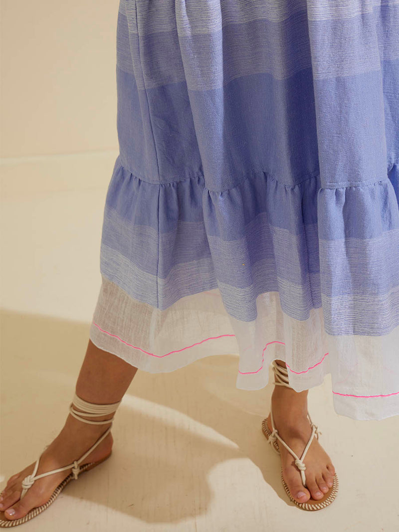 Close up on the legs of a woman wearing the Jelba Long Flutter Dress featuring gradient color block design of nine shades of soft pink and blues highlighted by a bright pink mini stripe at the edge of the dress.
