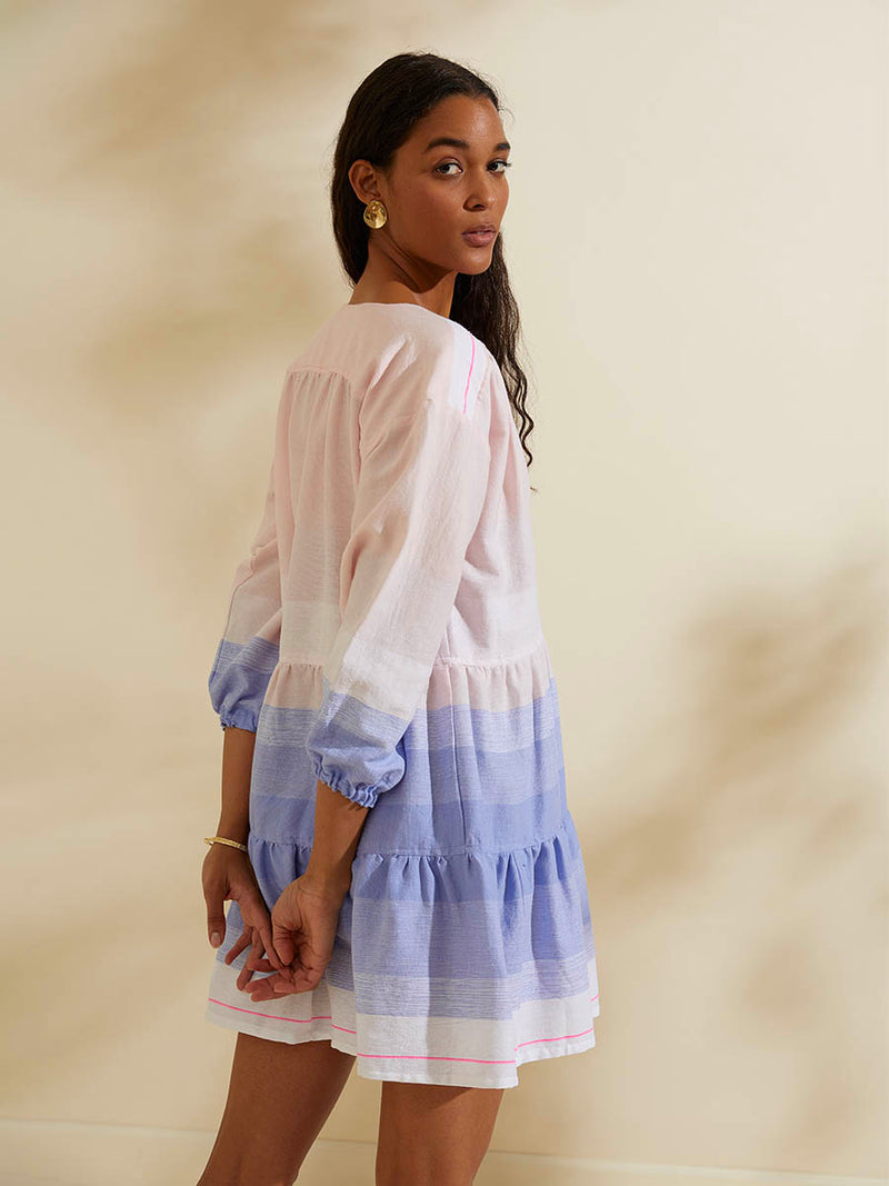 Back view of a woman standing wearing the Jelba Popover Dress featuring gradient color block design of nine shades of soft pink and blues highlighted by a bright pink mini stripe at the edge of the dress.