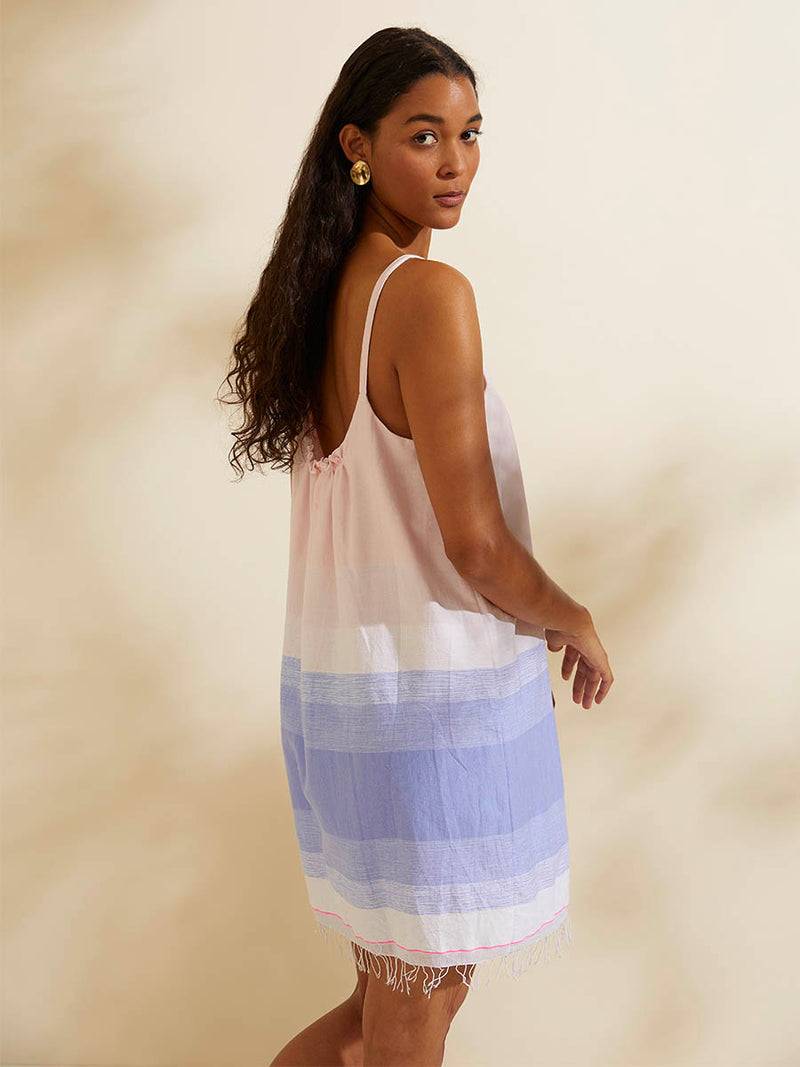 Back view of a woman standing wearing the Jelba Swing Dress featuring gradient color block design of nine shades of soft pink and blues highlighted by a bright pink mini stripe at the edge of the dress.