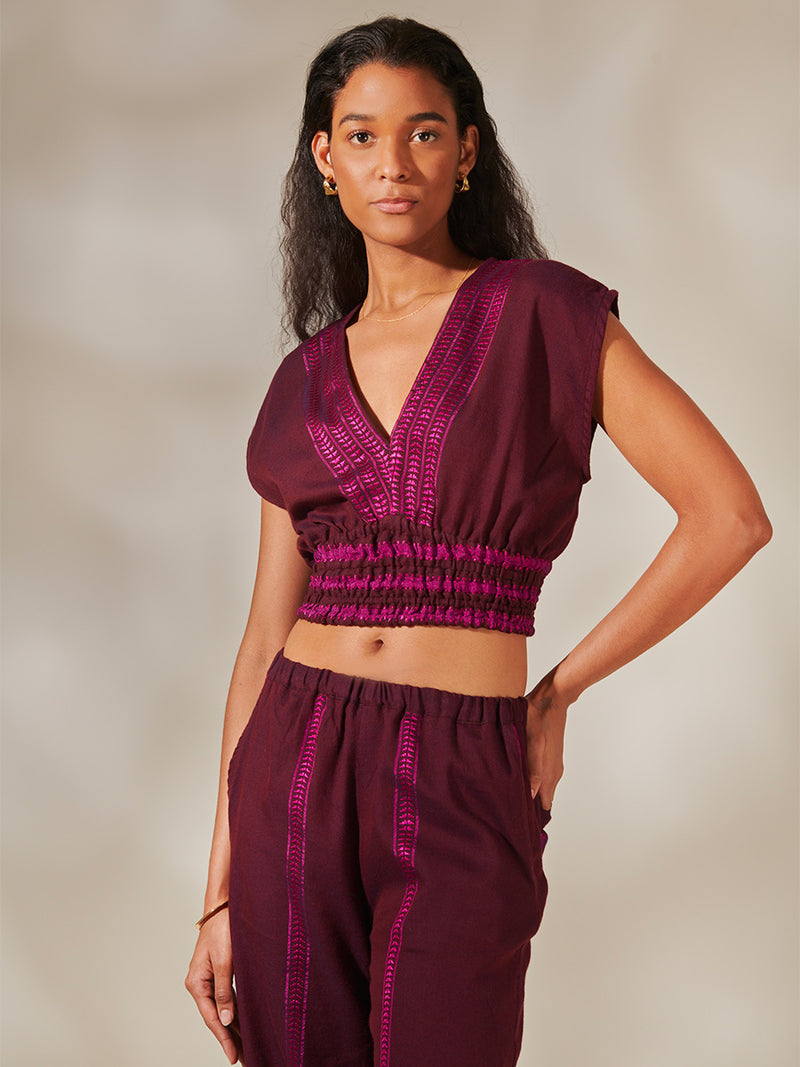 Woman Standing Wearing Alia Plunge Top and Jordanos Desta Pants featuring rich, luxurious burgundy tones with hints of magenta 