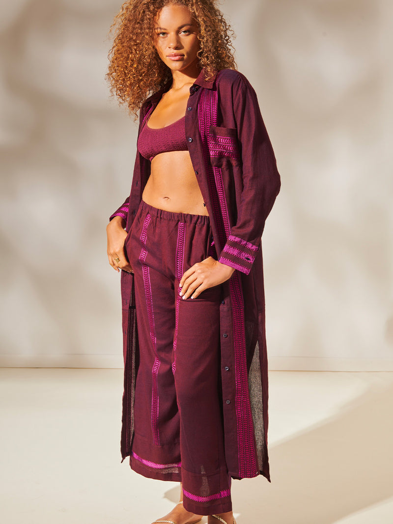 Woman Standing wearing Anata Shirt Dress and Desta Pants featuring rich, luxurious burgundy tones with hints of magenta, jordanos Burgundy Scoop Top and high Waist Bikini Bottom