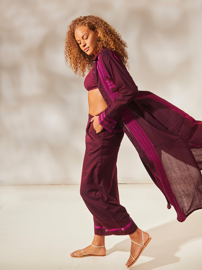 Side View of a Woman Standing wearing Anata Shirt Dress and Desta Pants featuring rich, luxurious burgundy tones with hints of magenta, jordanos Burgundy Scoop Top and high Waist Bikini Bottom