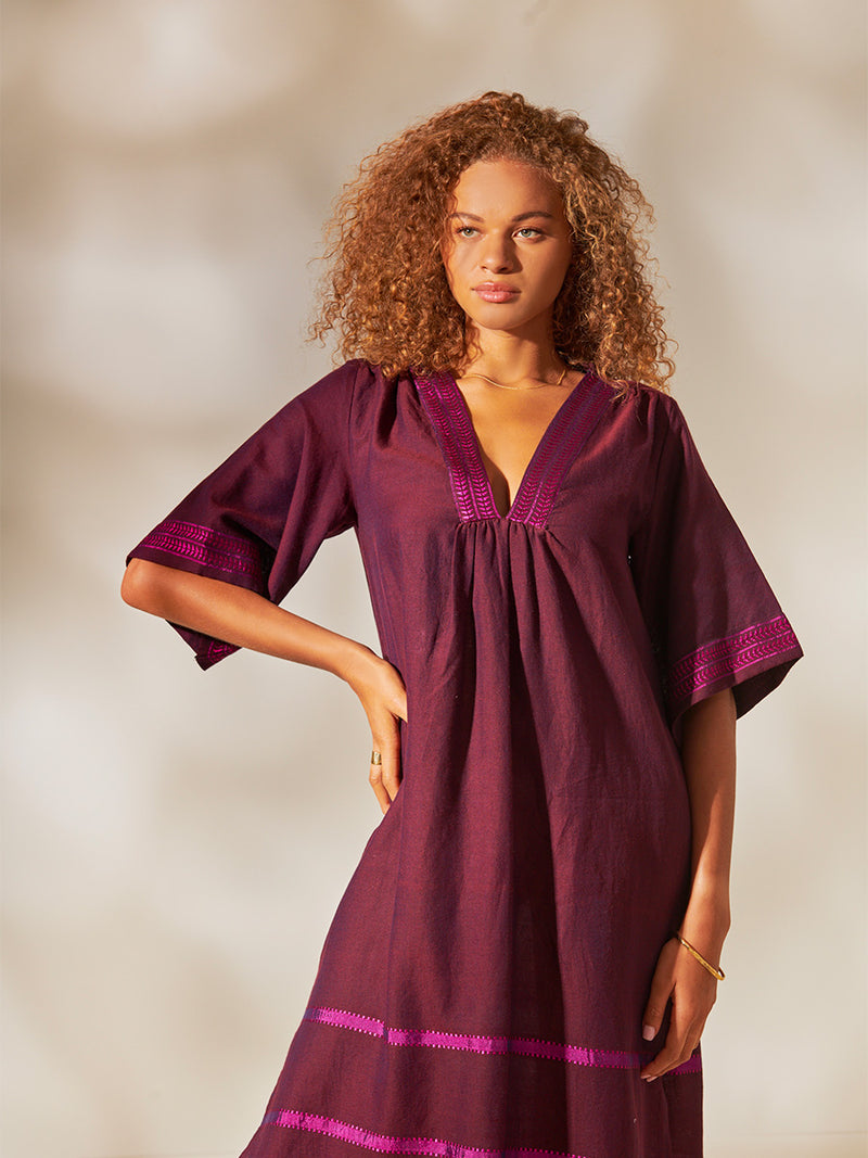 Woman Standing wearing Edna V Neck Dress featuring rich, luxurious burgundy tones with hints of magenta