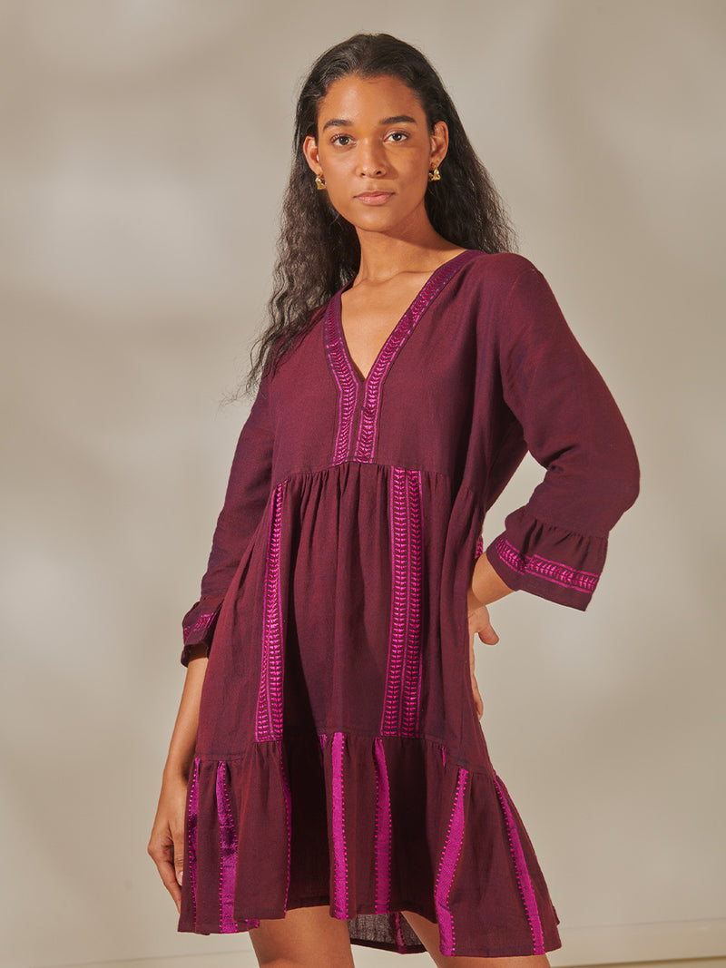 Woman Standing wearing Hanna Flutter Dress featuring rich, luxurious burgundy tones with hints of magenta