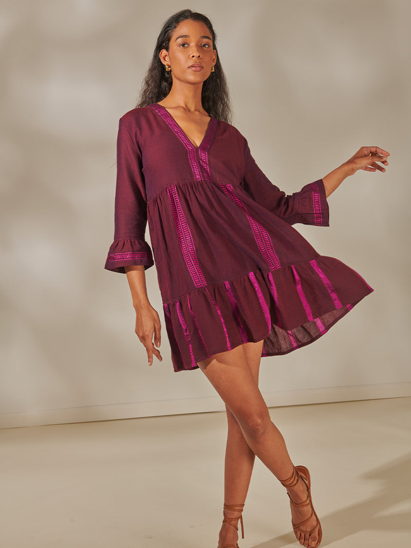 Woman Standing wearing Hanna Flutter Dress featuring rich, luxurious burgundy tones with hints of magenta