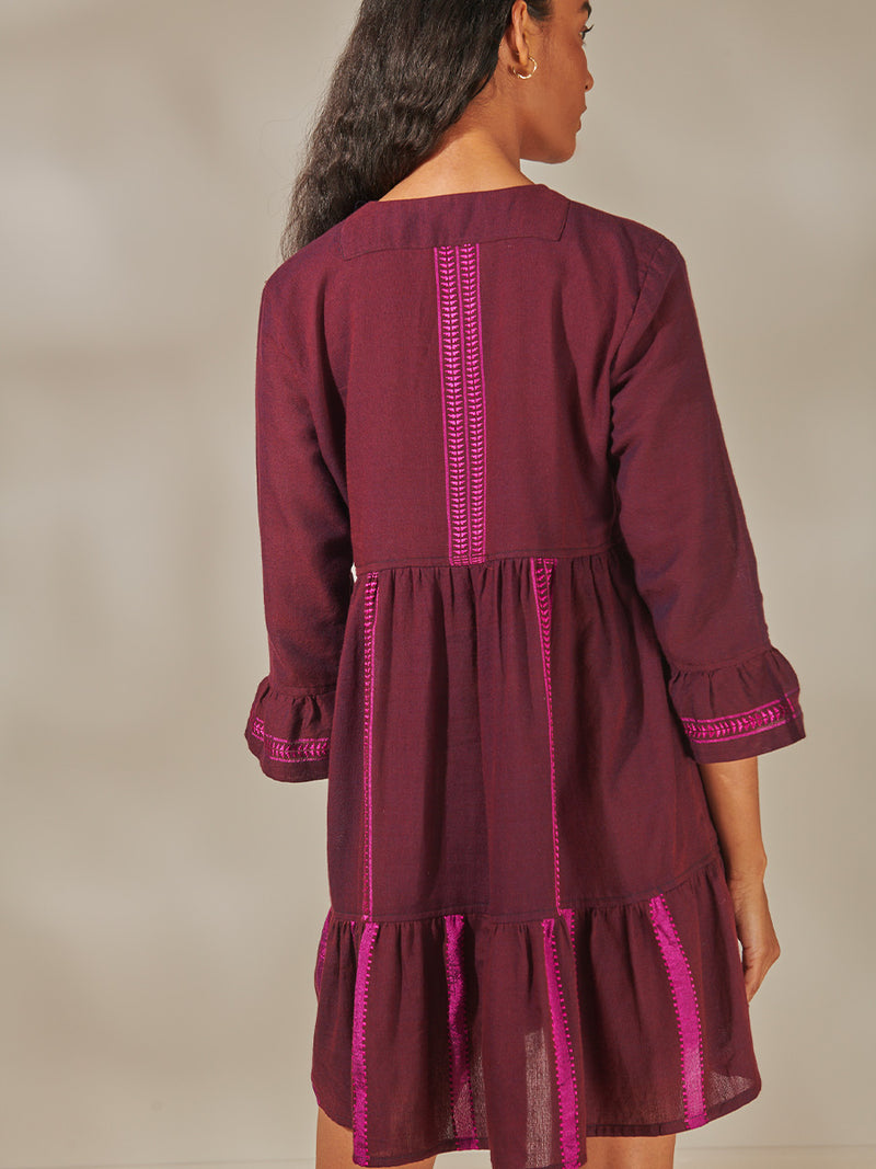 Back of a Woman Standing wearing Hanna Flutter Dress featuring rich, luxurious burgundy tones with hints of magenta
