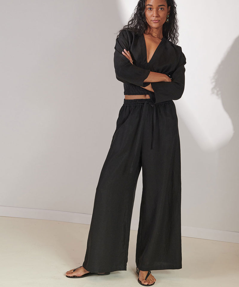 Woman standing with her arm crossed over her chest wearing the lemlem crop top and matching desta pants in black linen tencel.