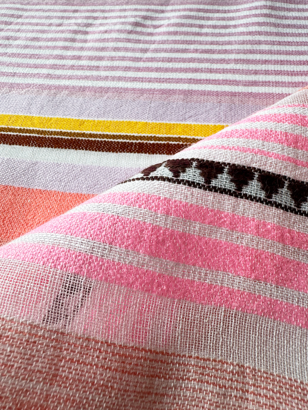 Close up on lemlem handwoven KIREMITI fabric featuring intricate stripe pattern interlaced with delicate mini Tibeb detailing, expressed in a soft yet vivid palette of cool pink, warm tangerine, rose, orchid, and accents of peach and deep burgundy.