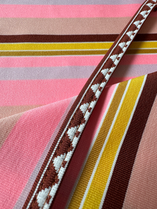 Close up on lemlem swim KIREMITI Pattern featuring intricate stripe pattern interlaced with delicate mini Tibeb detailing, expressed in a soft yet vivid palette of cool pink, warm tangerine, rose, orchid, and accents of peach and deep burgundy.