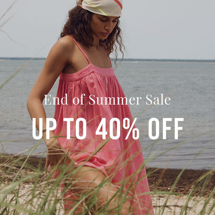 A woman wearing a pink sleeveless dress and a cream cap stands on a beach with grass in the foreground and water behind her. Large white text across the center reads 'End of Summer Sale UP TO 40% OFF'.
