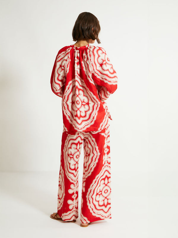 Back of a Woman Standing Wearing lemlem Desta Pants featuring custom-designed print inspired by ancient architectural patterns in rich, vibrant red and creamy ivory colors and a matching blouse