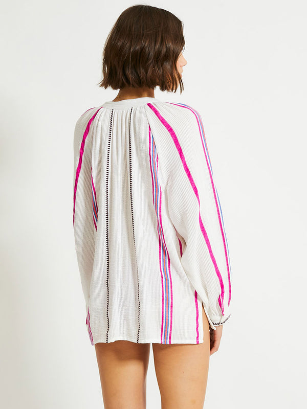 Back of a Woman Standing Wearing lemlem MITA Blouse featuring stripe pattern of bright magenta, blue, and orange on s crispy white background