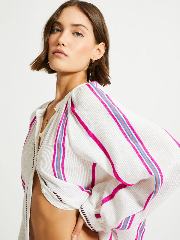 Woman Standing Wearing lemlem MITA Blouse featuring stripe pattern of bright magenta, blue, and orange on s crispy white background