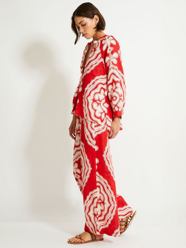 Side of a Woman Standing Wearing lemlem Desta Pants featuring custom-designed print inspired by ancient architectural patterns in rich, vibrant red and creamy ivory colors and a matching blouse