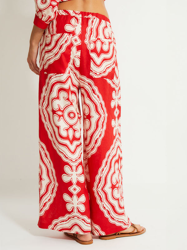 Back Close up on Woman's legs Standing Wearing lemlem Desta Pants featuring custom-designed print inspired by ancient architectural patterns in rich, vibrant red and creamy ivory colors and a matching blouse