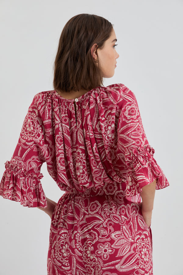 Back of a Woman Standing Wearing lemlem MONIKA Blouse and DESTA Pants featuring rich ruby-red fabric  adorned with intricate white floral and leaf motifs print