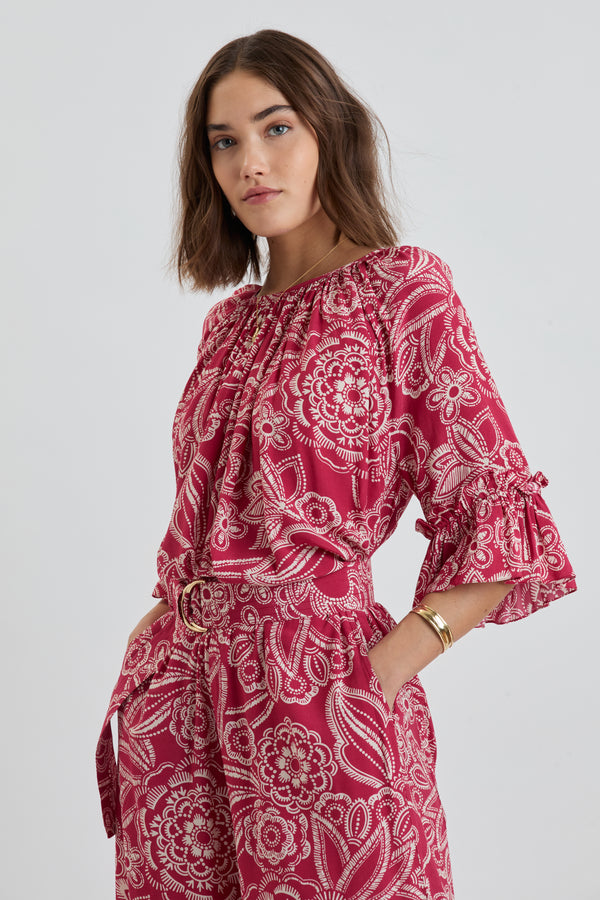 Woman Standing Wearing lemlem MONIKA Blouse and DESTA Pants featuring rich ruby-red fabric  adorned with intricate white floral and leaf motifs print