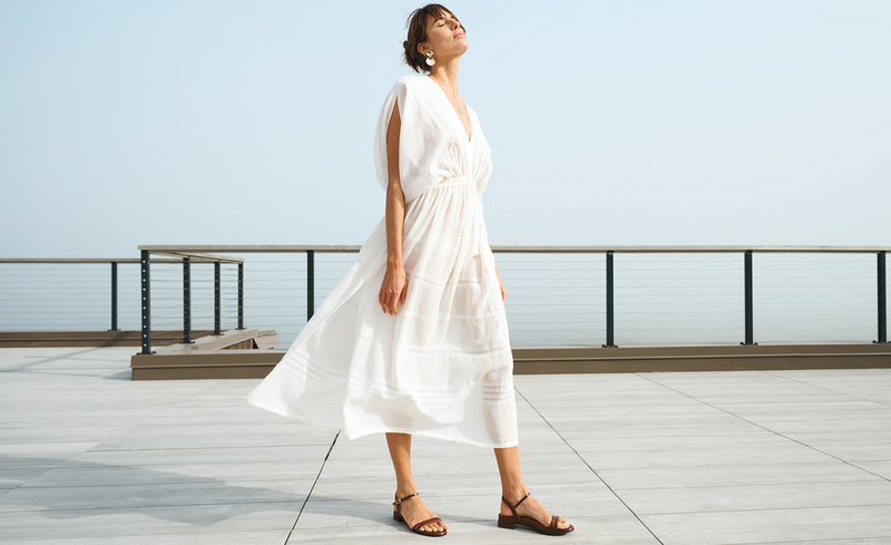 Woman in a cream lemlem handwoven LEILA  dress standing on a deck with a clear sky background