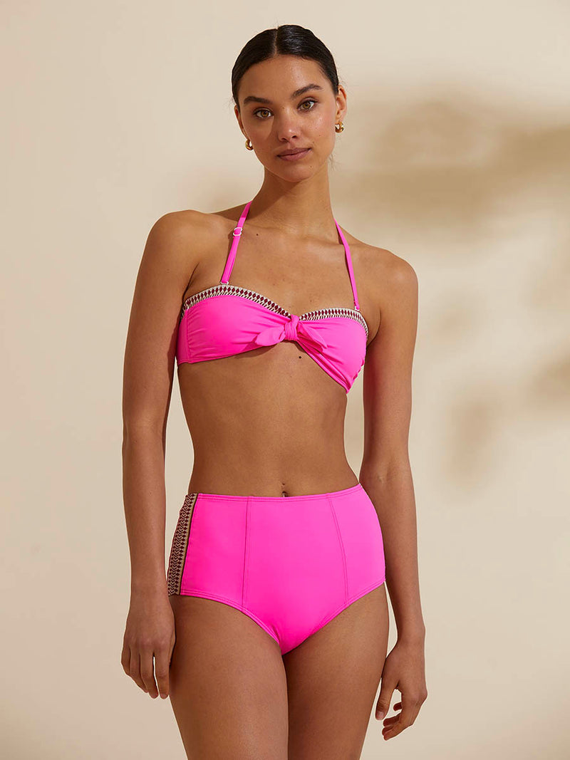 Woman standing wearing the Lena High Waisted Bikini Bottom in bright neon pink with a bordeaux diamond trim.