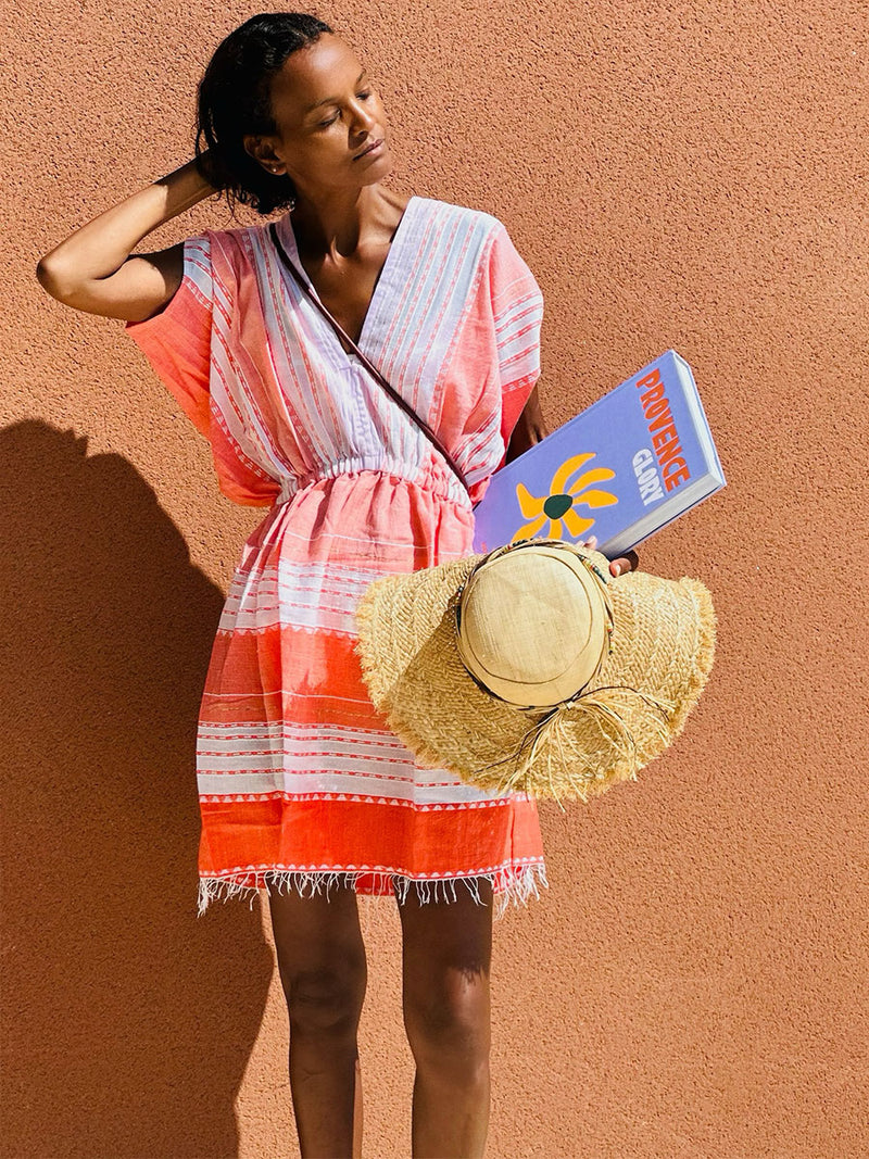 Liya Kebede standing holding a book and a hat in her hand wearing Eshal Short Plunge Neck Dress