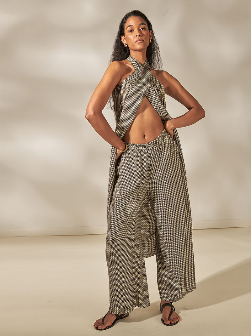 Woman Standing Wearing Adia Sarong Featuring diamond Tibeb pattern stripes in earthy brown & natural colors wrapped around her chest and Mediri Brown Desta Pants