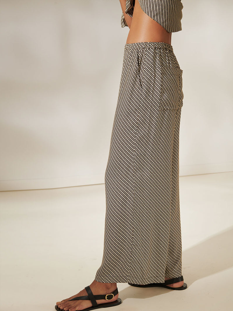 Close Up of a Woman Standing Wearing Adia Sarong Wrapped around her neck and Desta Wide Leg Pants Featuring diamond Tibeb pattern stripes in earthy brown & natural colors.