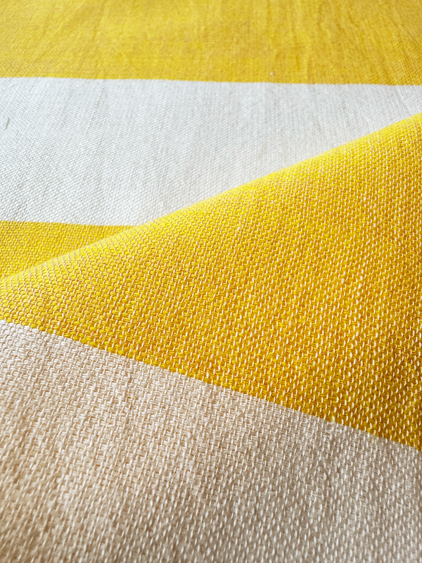 Close up on lemlem handwoven fabric featuring a wide block stripe pattern in rich yellow on a creamy vanilla background.