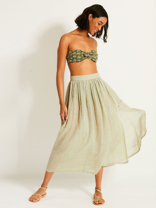 Woman Standing Wearing lemlem FREYE Skirt featuring airy gauze fabric in a delicate earthy sage color